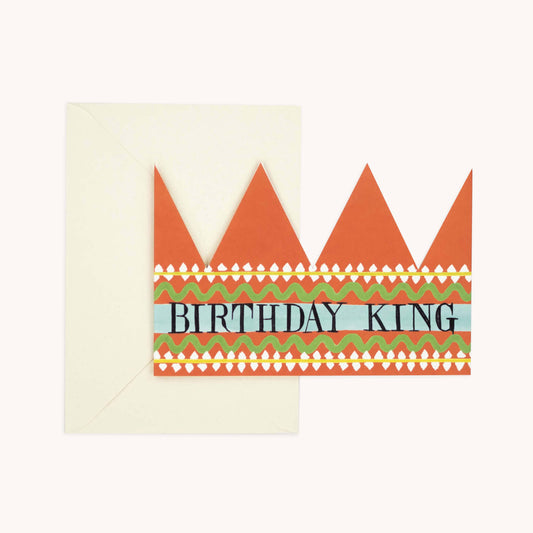 Orange party hat crown card with a striped patterned band reading 'BIRTHDAY KING' in black, cream envelope behind