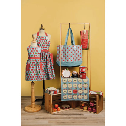 Yellow-toned lifestyle scene styled with an apple-print jacquard towel, matching apron, tote bag, and mugs – PABOOM