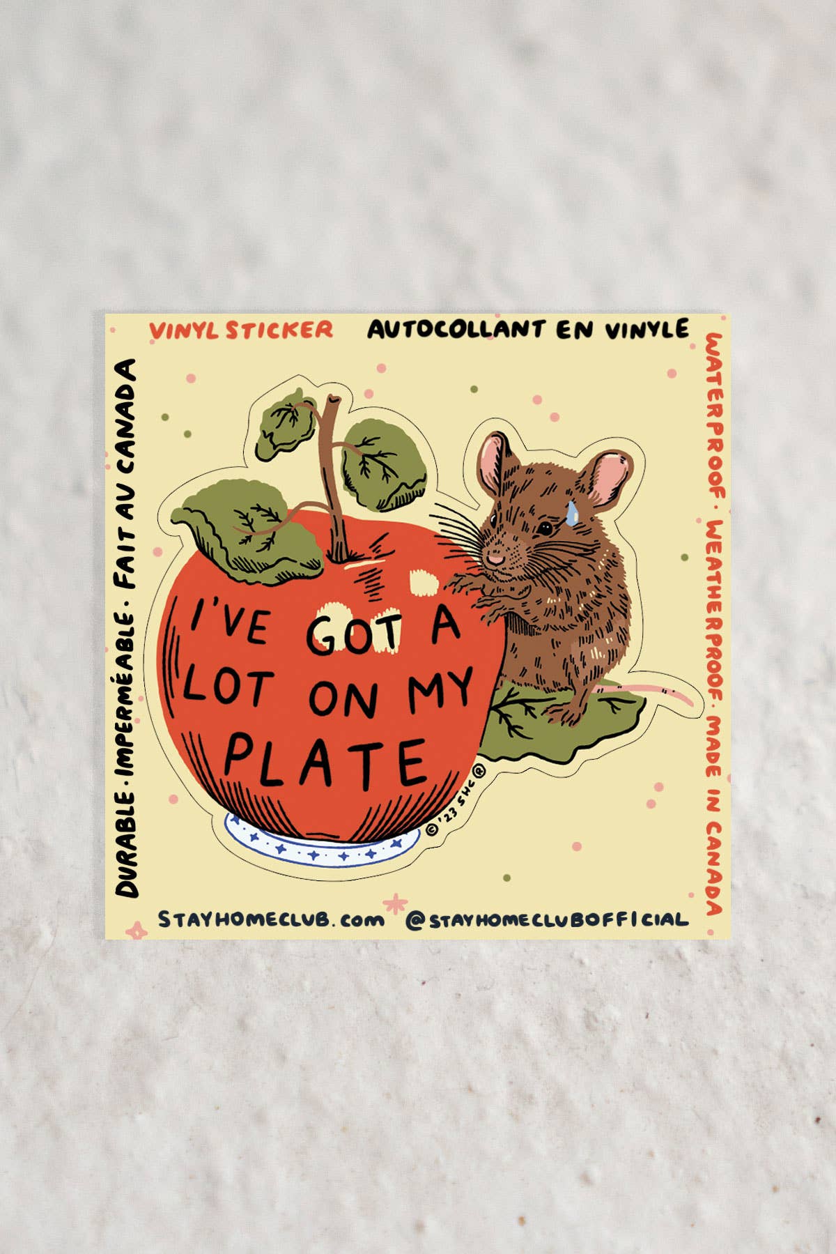 Vinyl sticker of an illustrated mouse next to a red apple reading 'I've Got a Lot on My Plate,' on a bilingual branded backing marked Fait au Canada