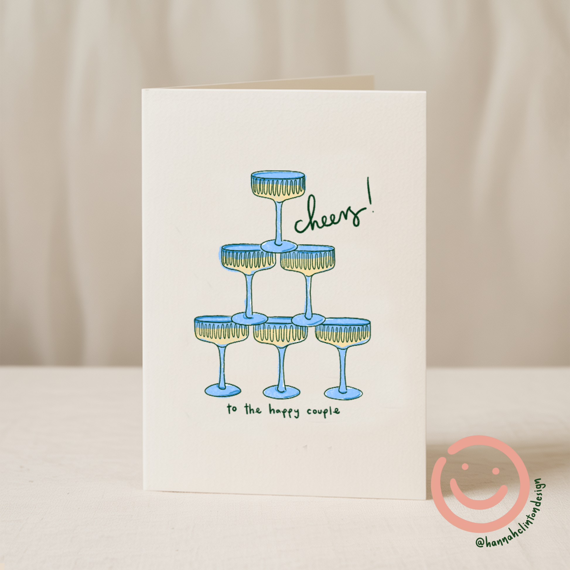 Blue Iris Designs Co wedding card illustrated with a stacked pyramid of blue champagne coupes and "cheers! to the happy couple" text - PABOOM