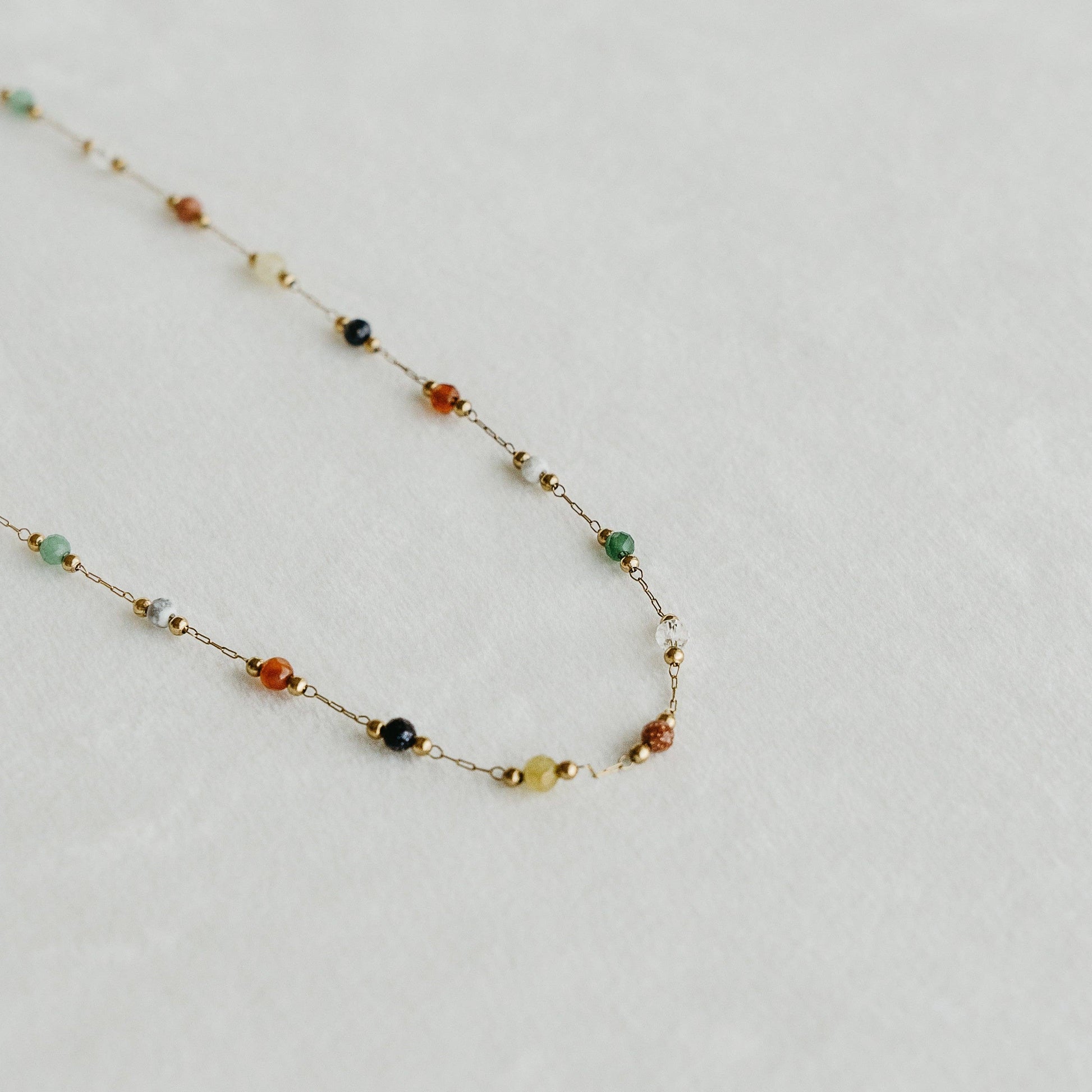 Esme necklace with colourful gemstone beads on a fine gold chain, laid on a light surface - PABOOM