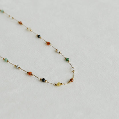 Esme necklace with colourful gemstone beads on a fine gold chain, laid on a light surface - PABOOM