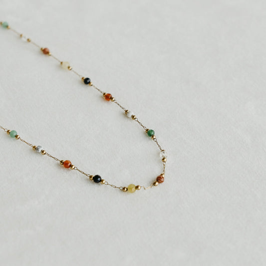 Esme necklace with colourful gemstone beads on a fine gold chain, laid on a light surface - PABOOM