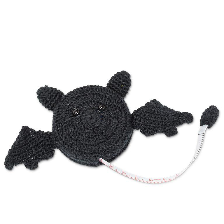 Black crochet bat-shaped tape measure with stitched button eyes and textured wings, tape extended to show measurement markings.