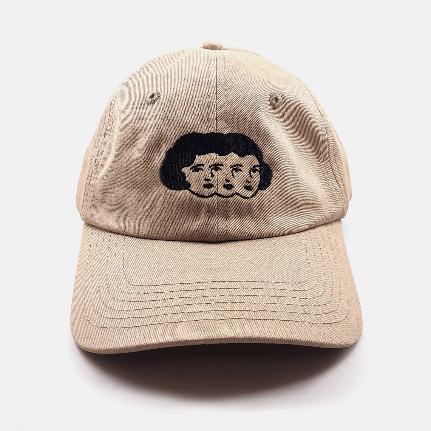 Tan dad hat with an embroidered design of three faces sharing one head of hair - PABOOM