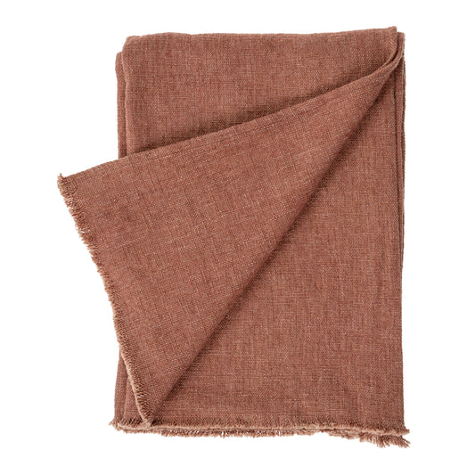 Rust-brick woven linen blanket with fringed edges, draped over the end of a bed