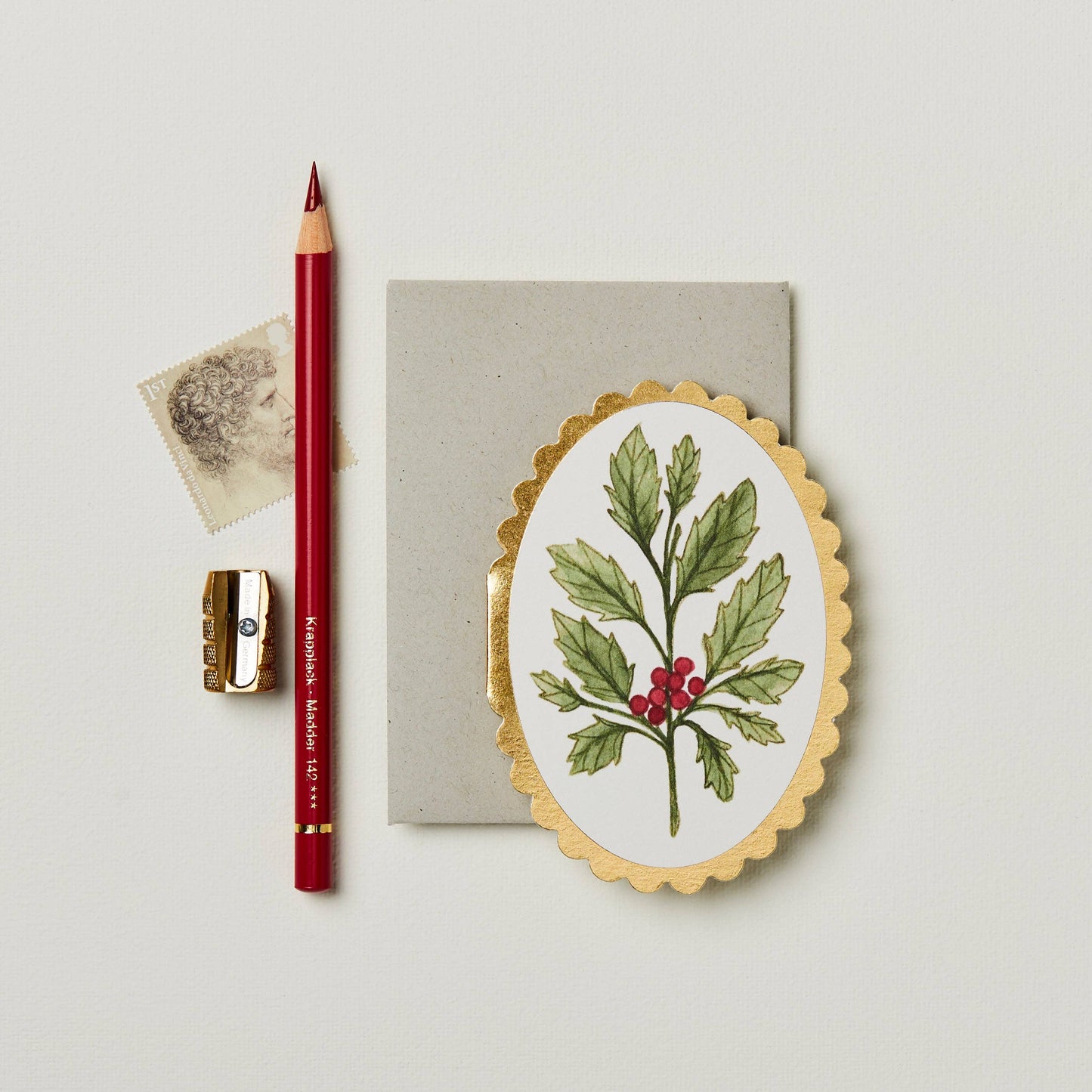 Green holly leaves with red berries on cream oval mini card with gold scalloped edge