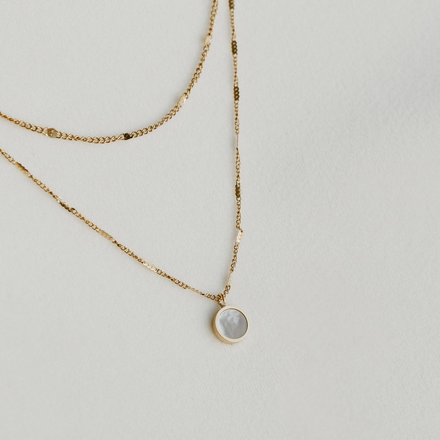 Liora double-layered gold necklace with a round pendant, laid on a light surface - PABOOM