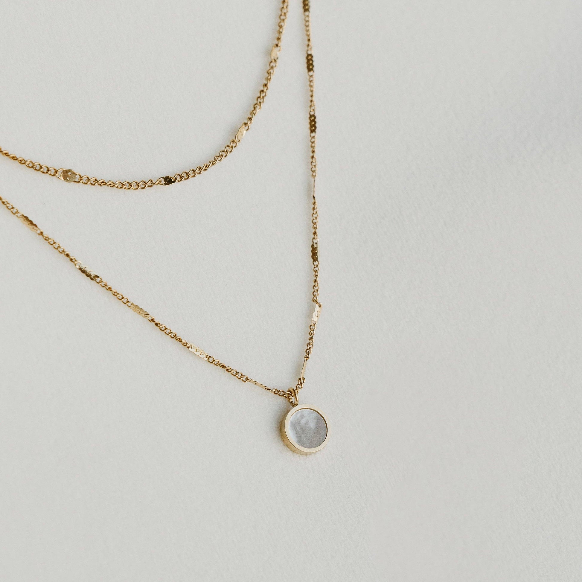 Liora double-layered gold necklace with a round pendant, laid on a light surface - PABOOM