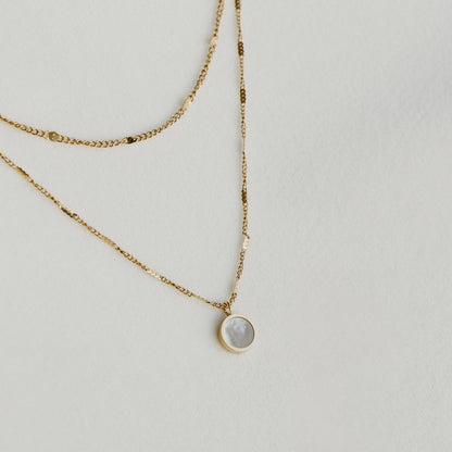 Liora double-layered gold necklace with a round pendant, laid on a light surface - PABOOM