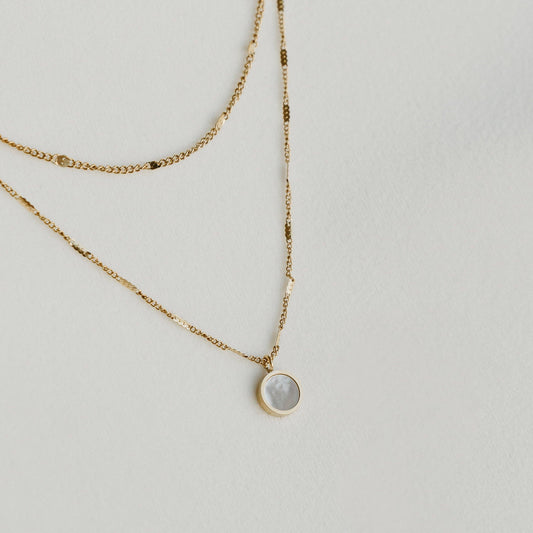 Liora double-layered gold necklace with a round pendant, laid on a light surface - PABOOM
