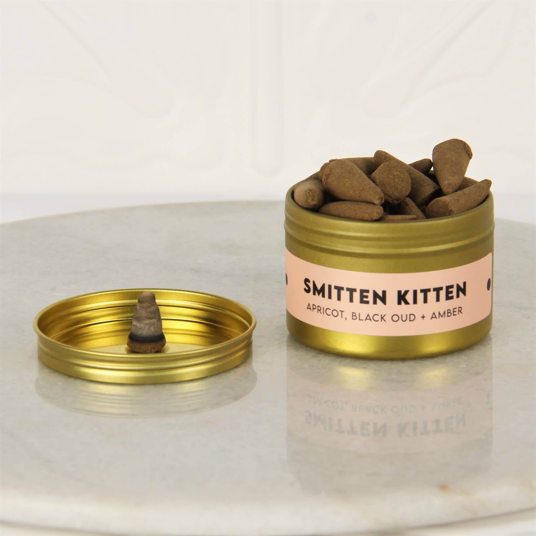 Open gold tin of Charleston & Harlow Smitten Kitten incense cones with peach label, a cone resting on the lid