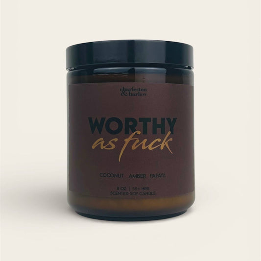 Charleston & Harlow Worthy As Fuck soy candle in amber glass jar with dark mauve label and gold script