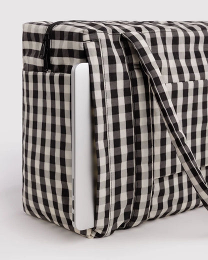 Model carrying the BAGGU Small Cloud Carry-On in black and cream gingham over one shoulder