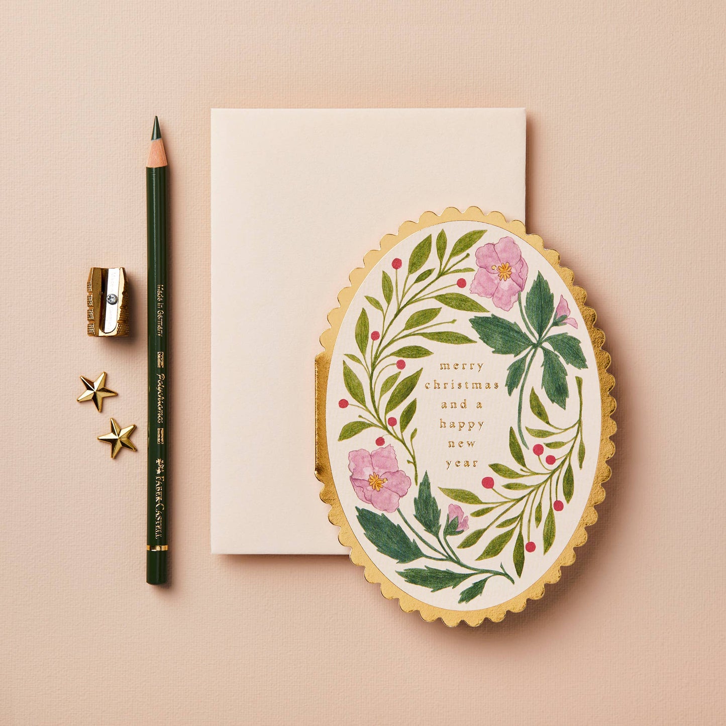 Pink floral wreath with red berries on oval card with gold scalloped edge, reading Merry Christmas and a Happy New Year
