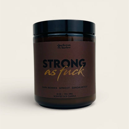Charleston & Harlow Strong As Fuck soy candle in amber glass jar with dark brown label and gold script