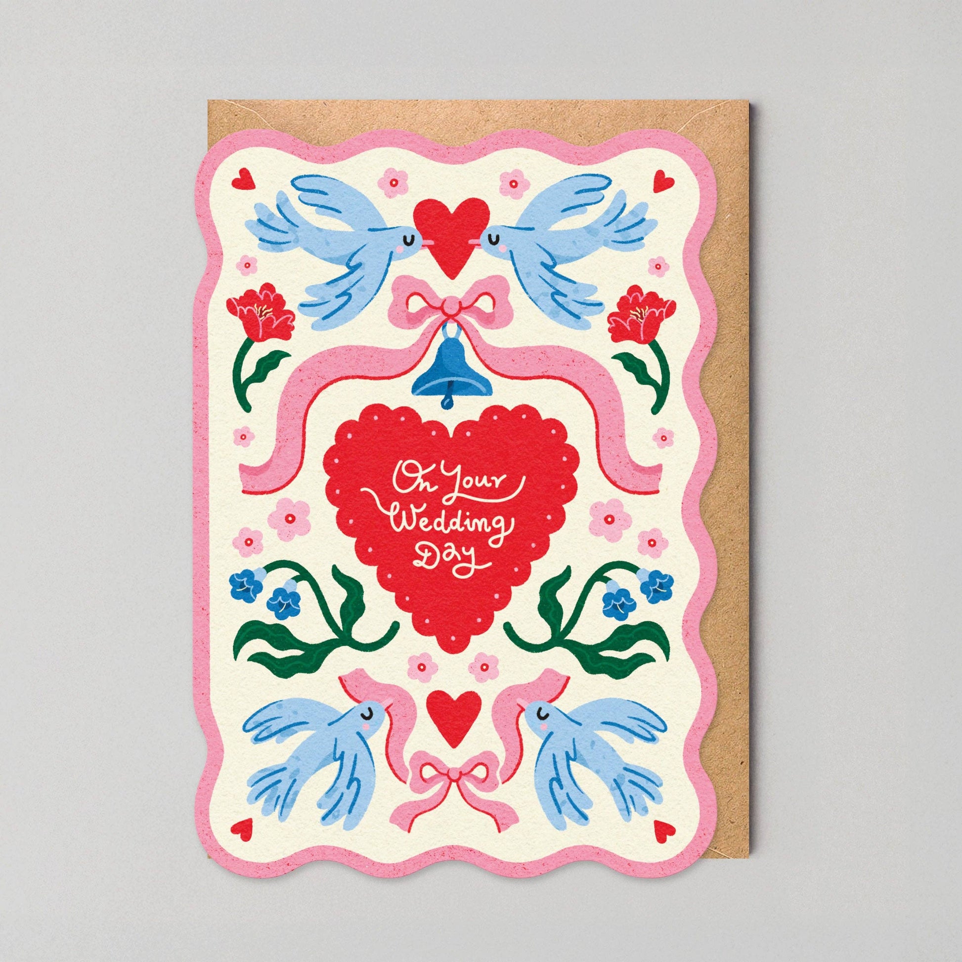 Scalloped-edge wedding greeting card with pink border, illustrated lovebirds, a ribbon-tied bell, and a red heart reading "On Your Wedding Day."