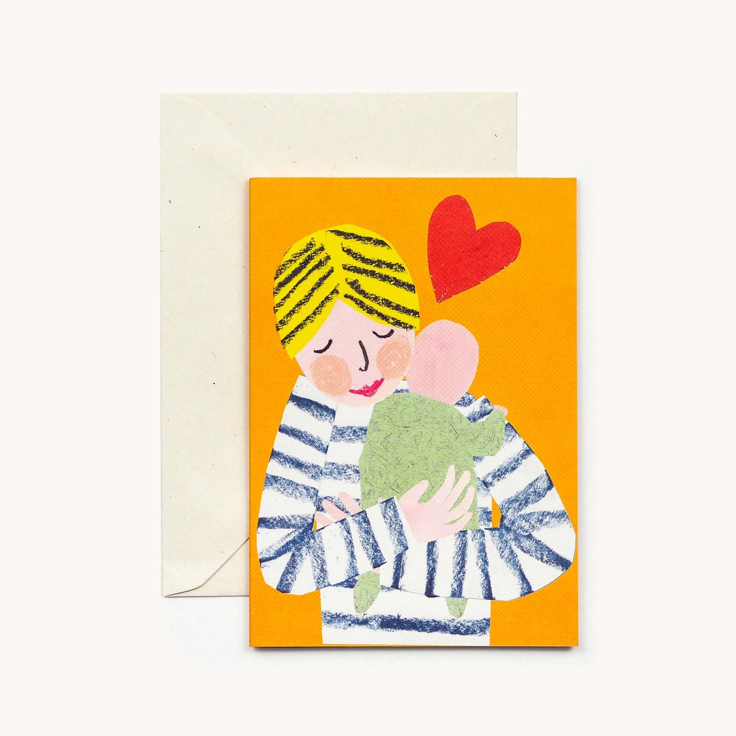 Orange greeting card with an illustrated blonde parent in a striped jumper cuddling a swaddled baby, a red heart above, brown envelope behind