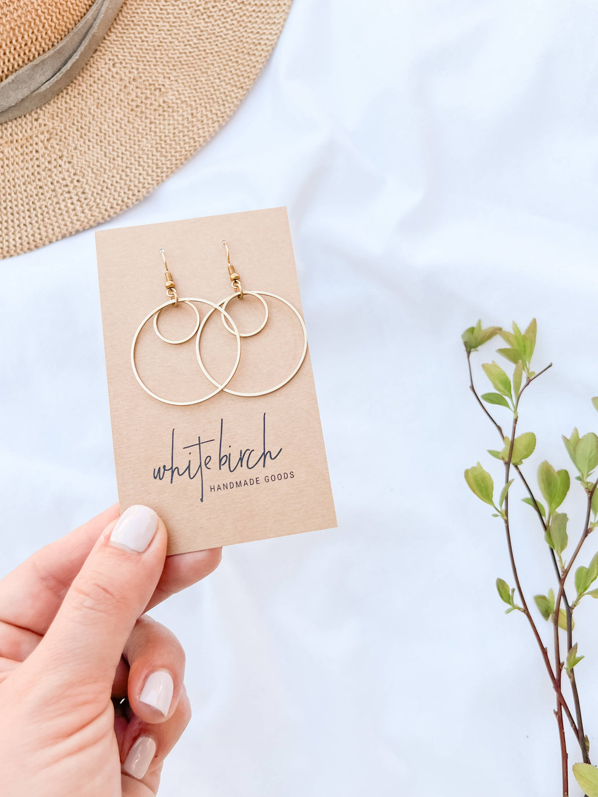 Hand holding brass double circle earrings on a Whitebirch Handmade Goods earring card