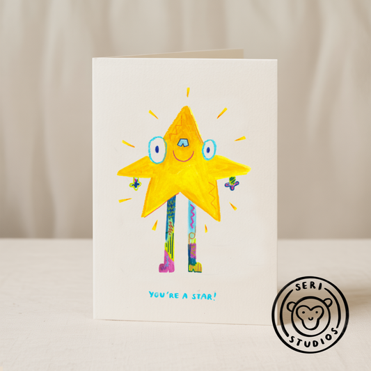 Blue Iris Designs Co card featuring a smiling yellow star character with colorful striped legs and "You're A Star!" text, Seri Studios monkey logo bottom right - PABOOM