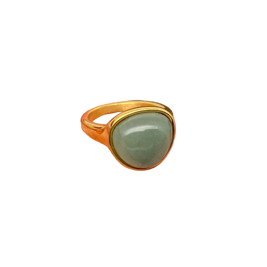 Gold ring with a green stone on a finger against a gray background
