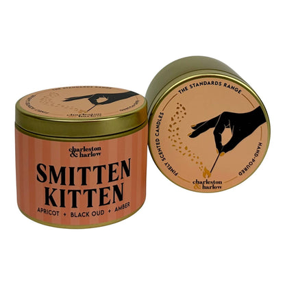 Gold travel tin soy candle with peach striped Smitten Kitten label, shown open beside its lid with hand-poured icon