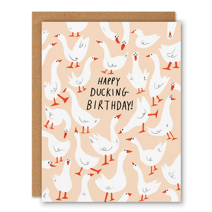 Peach birthday card covered in white geese with orange feet and Happy Ducking Birthday lettering - PABOOM