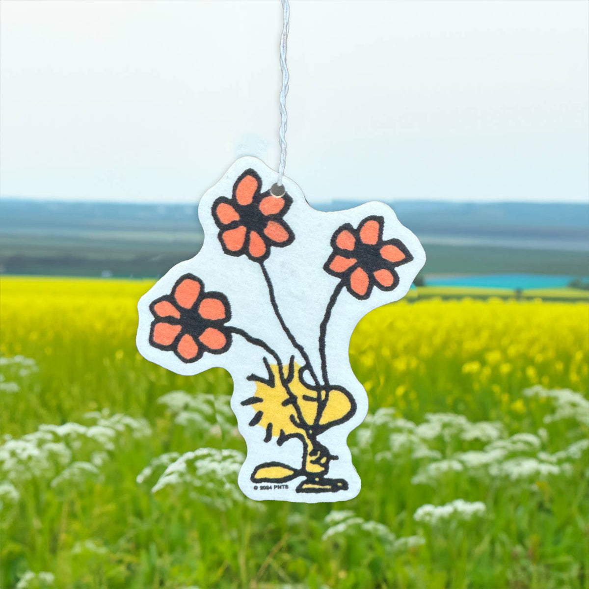Close-up of the Woodstock flower air freshener showing its summer scent label and hanging elastic band.