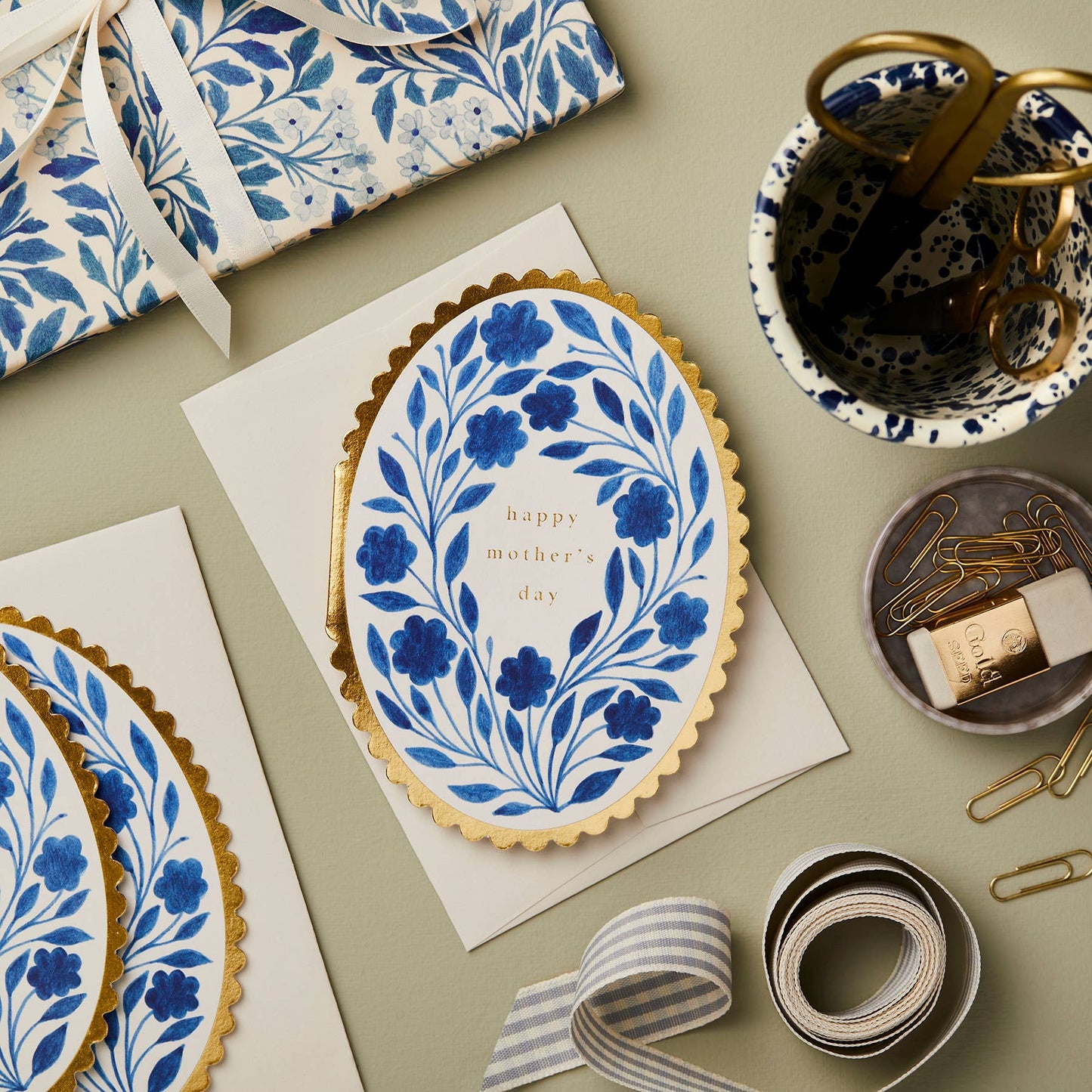 Blue delft-style floral wreath on white oval card with gold scalloped edge, reading Happy Mother's Day