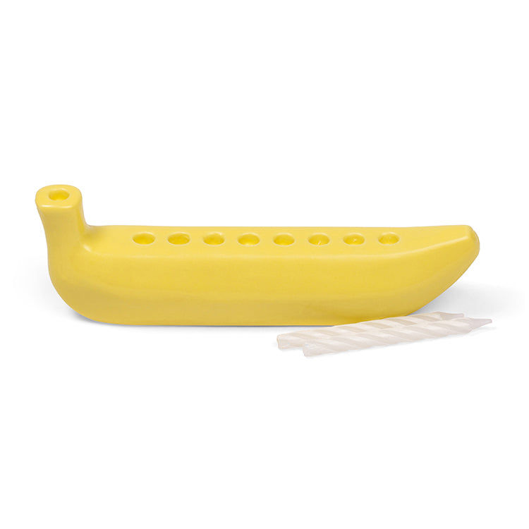 Small yellow ceramic banana-shaped menorah with nine candle holes, shown beside a row of thin white candles.