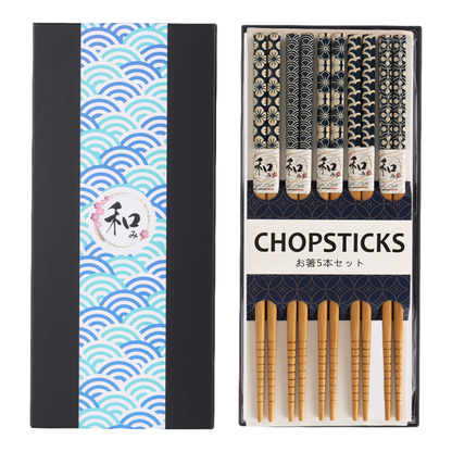 Five pairs of bamboo chopsticks in coordinating Japanese-pattern sleeves labeled Nagomi, packaged beside a black and teal wave-print gift box