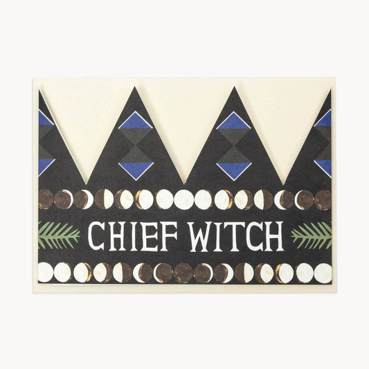 Black party hat crown card with a blue diamond pattern, a row of moon-phase circles, and the text 'CHIEF WITCH' in white flanked by green fern illustrations
