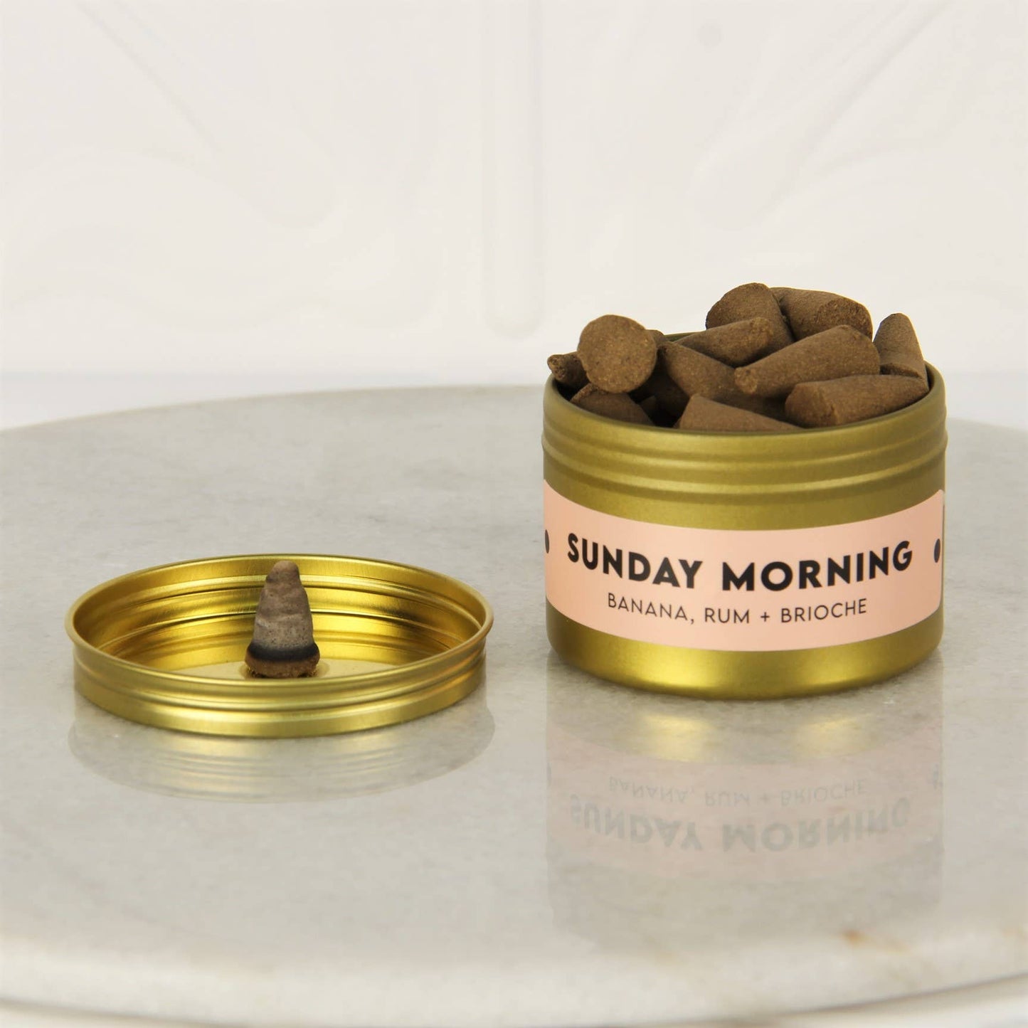 Open gold tin of Charleston & Harlow Sunday Morning incense cones with peach label, a cone resting on the lid