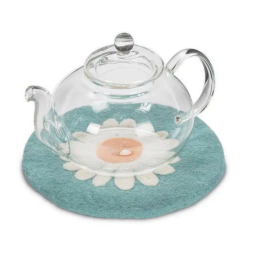 Glass teapot resting on blue daisy-shaped felt wool trivet – heat protection with floral style - PABOOM