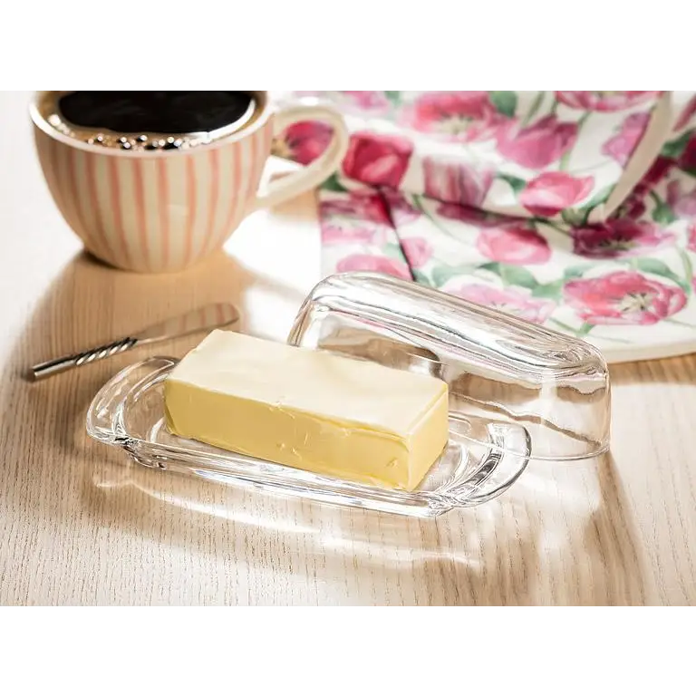 Glass butter dish with stick of butter on table beside coffee and floral napkin – simple and elegant serving - PABOOM