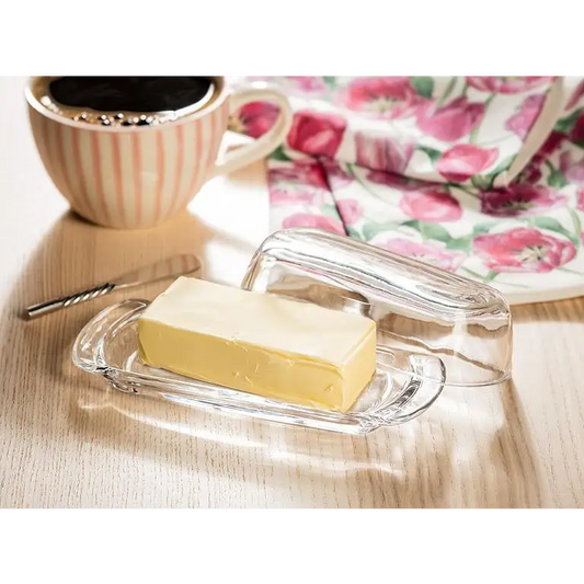 Glass butter dish with stick of butter on table beside coffee and floral napkin – simple and elegant serving - PABOOM