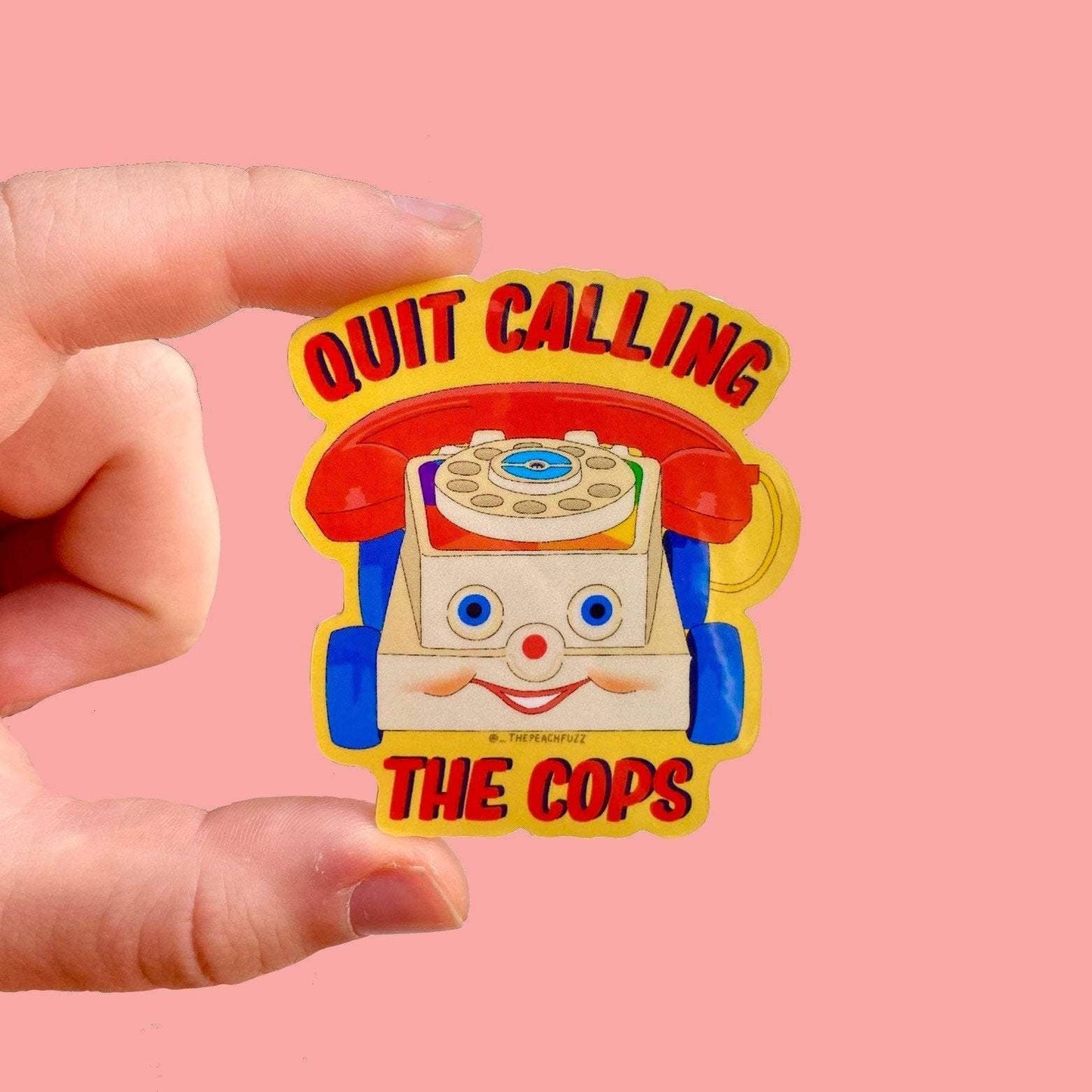 Illustrated retro chatter telephone toy with a smiling face, reading Quit Calling The Cops