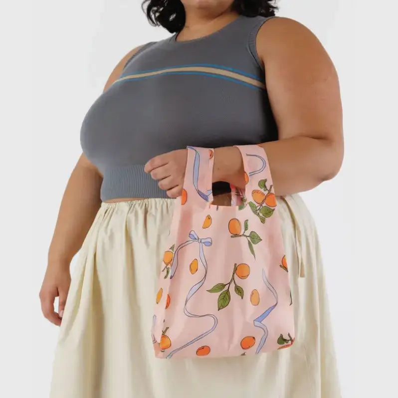 Baby Baggu bag featuring a pattern of apricots and ribbons being held on the arm - PABOOM