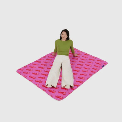 Person sitting on Pink Lobster Puffy Picnic Blanket laid out on grass - PABOOM