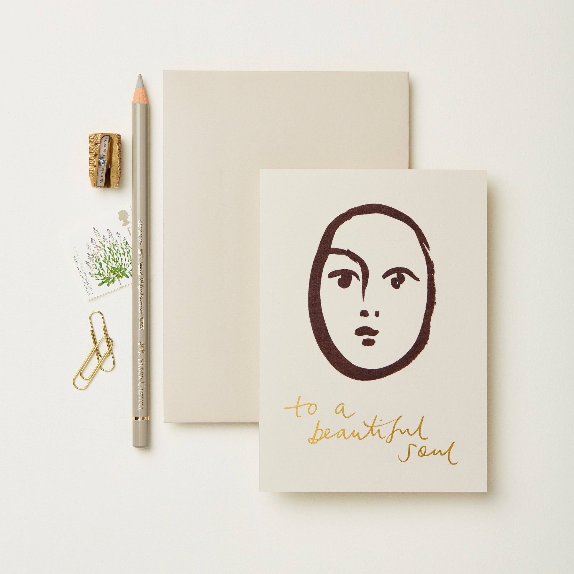 Cream card with a minimalist maroon line-art face illustration, reading To A Beautiful Soul in gold script