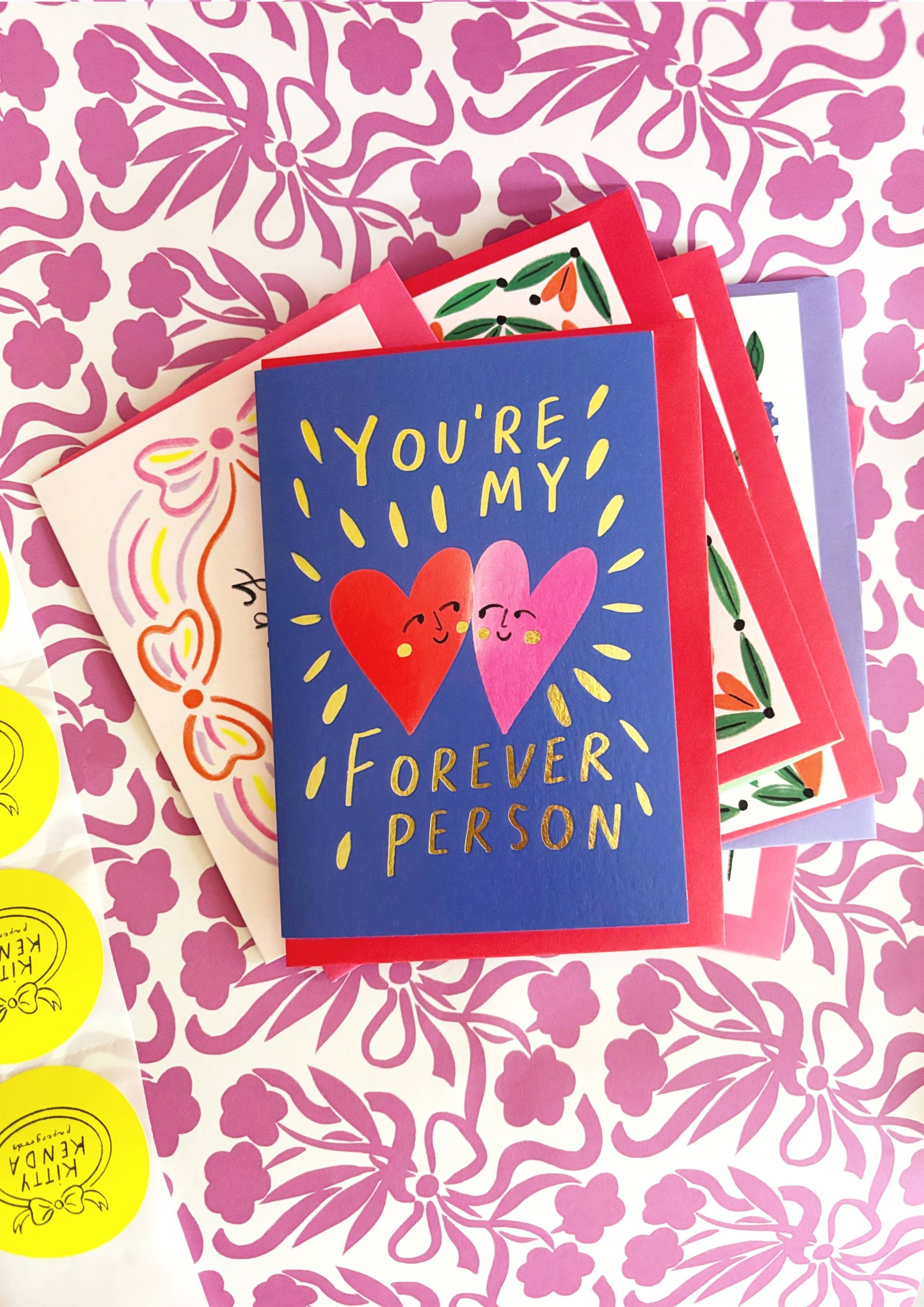 Kitty Kenda foiled love card with two smiling gold-foil hearts and "You're My Forever Person" text on navy background