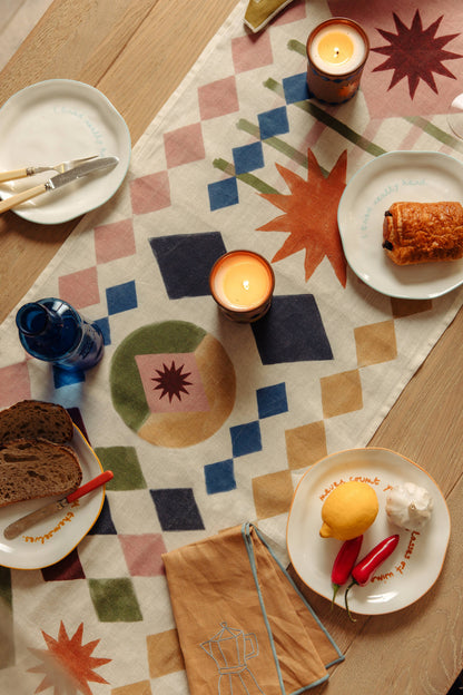 Dining table setting with plates, candles, and bread on a patterned tablecloth.