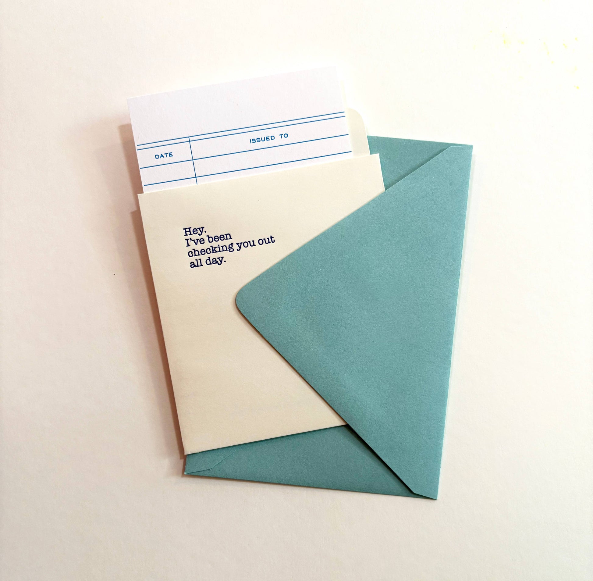Light ivory library checkout card reading Hey, I've been checking you out all day, peeking out of a teal envelope