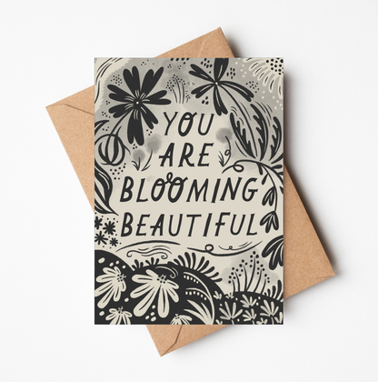 'You Are Blooming Beautiful' card featuring bold black botanical illustration and hand-lettered text on a cream background