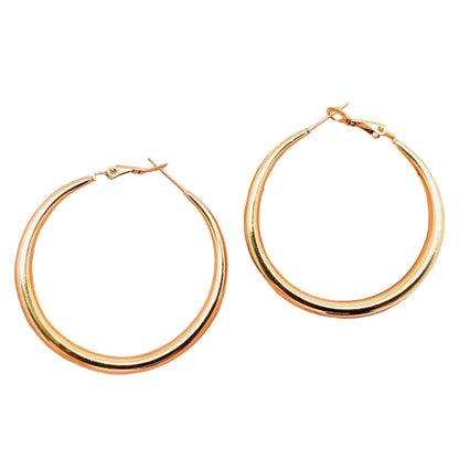 Gold hoop earrings held in a hand against a light background