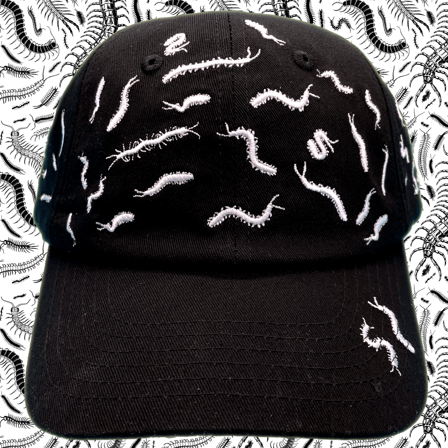 Black dad hat covered in white embroidered centipede designs scattered across the crown and brim, front view, with a centipede-print background.