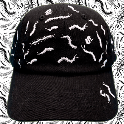 Black dad hat covered in white embroidered centipede designs scattered across the crown and brim, front view, with a centipede-print background.