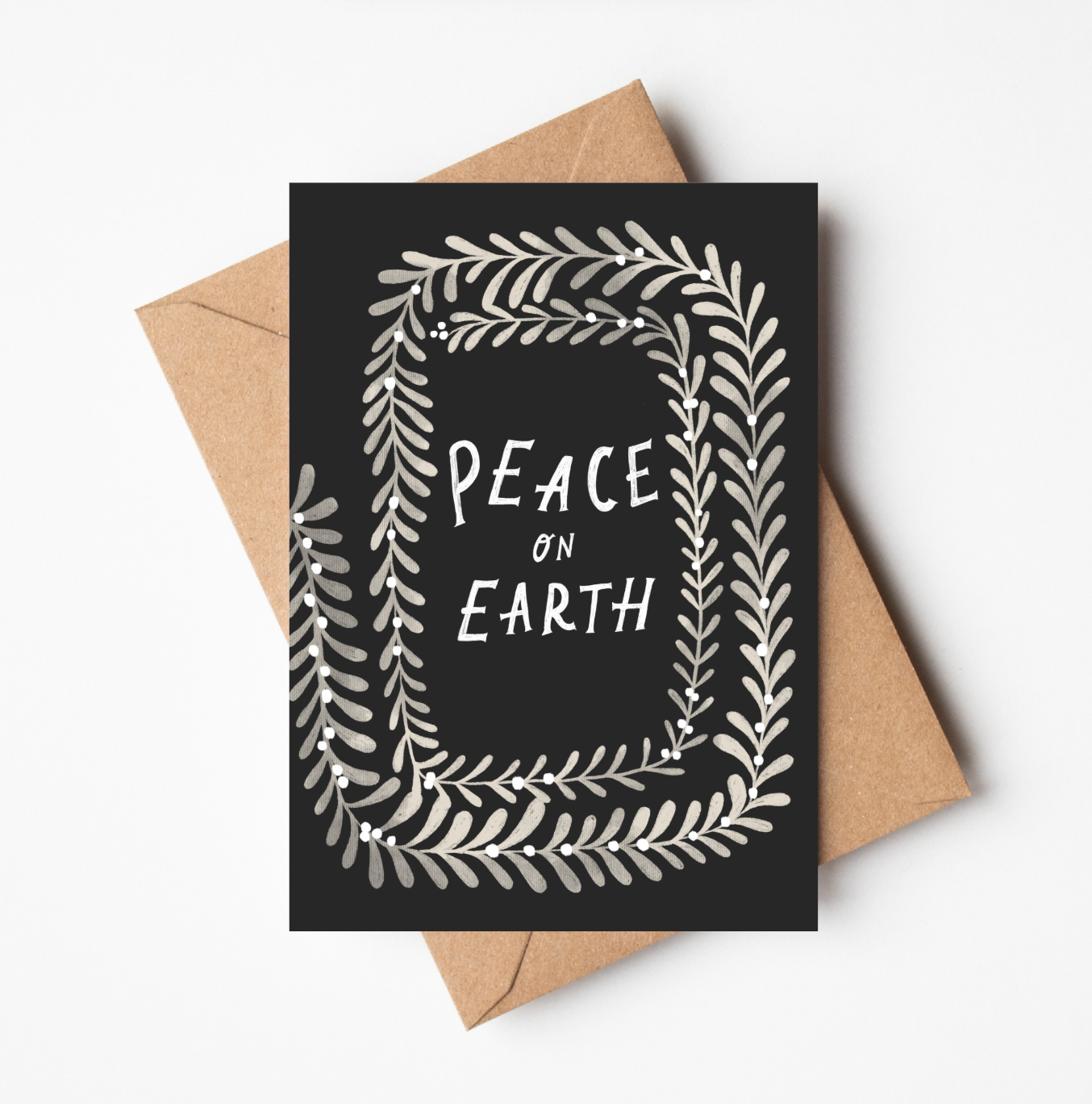 'Peace on Earth' Christmas card featuring a black background bordered by a cream botanical wreath, with 'PEACE ON EARTH' hand-lettered in the centre