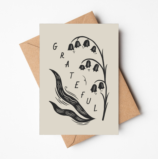 'Grateful' gratitude card with black and white botanical illustration of lily of the valley flowers and the word GRATEFUL in bold lettering, on a cream card