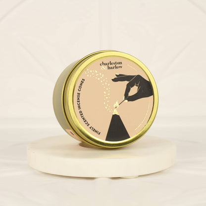 Closed gold tin lid of Charleston & Harlow incense cones with tan label featuring a hand-drawn cone illustration, one cone resting on top